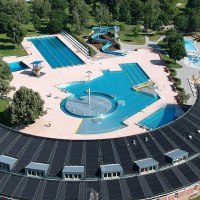 Luftaufnahme eines Freibads mit Becken, Rutschen und Solarzellen auf dem Dach. Umgeben von Bäumen und Sportplätzen., © Stadt Leonberg
