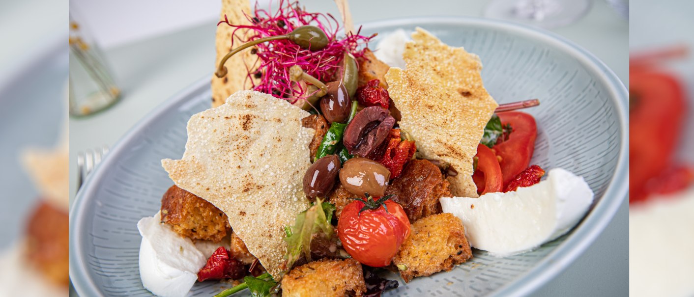 Mediterraner Salat mit Oliven, getrockneten Tomaten, Mozzarella, Croutons und knusprigen Chips auf einem Teller., © Marc Luppa