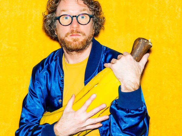 Ein Mann mit Brille und Bart in blauer Jacke h&auml;lt ein gro&szlig;es gelbes Objekt vor einem leuchtend gelben Hintergrund., &copy; Konzertkreis Triangel Compagnia Compostelli e.V.