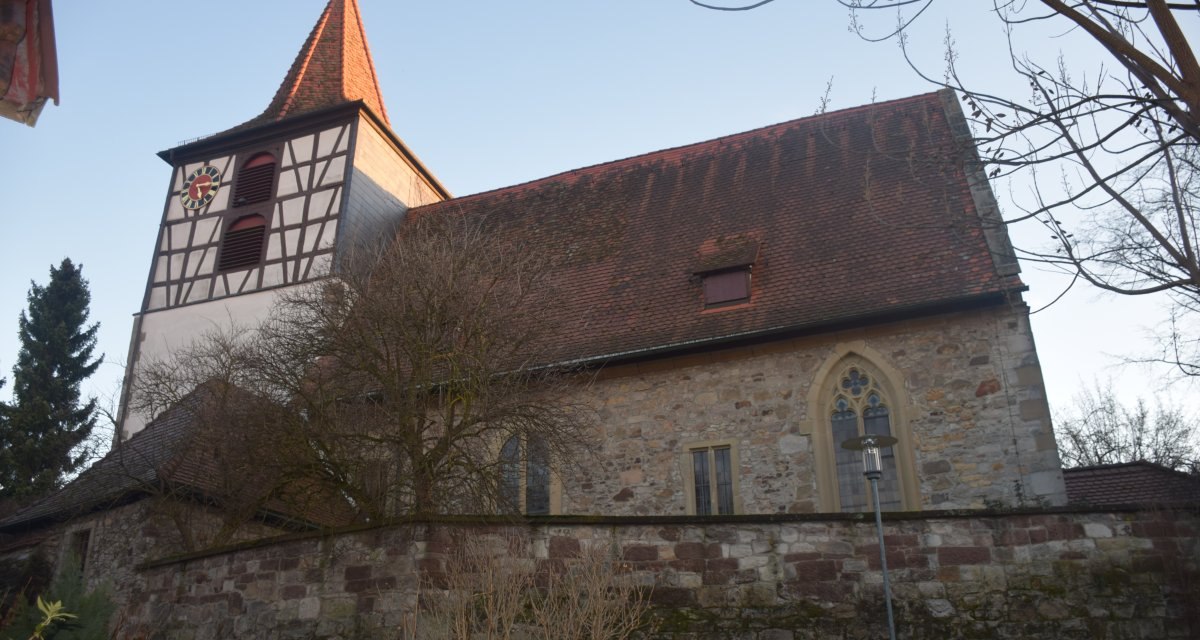 Die Evangelische St. Veitskirche mit Fachwerkturm und rotem Dach vor blauem Himmel, umgeben von Bäumen und einer Steinmauer., © Land der 1000 Hügel - Kraichgau-Stromberg Die Evangelische St. Veitskirche mit Fachwerkturm und rotem Dach vor blauem Himmel, umgeben von Bäumen und einer Steinmauer., © Land der 1000 Hügel - Kraichgau-Stromberg