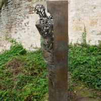Metallskulptur eines Menschen, der hinter einer Wand hervorschaut, vor einer alten Steinmauer und umgeben von Pflanzen., © Natur.Nah. Schönbuch & Heckengäu