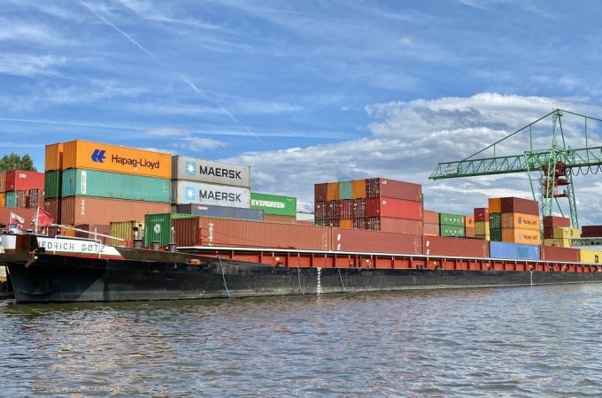 Ein Containerschiff im Stuttgarter Hafen mit bunten Containern und einem Kran im Hintergrund unter blauem Himmel., &copy; Stuttgart Marketing GmbH