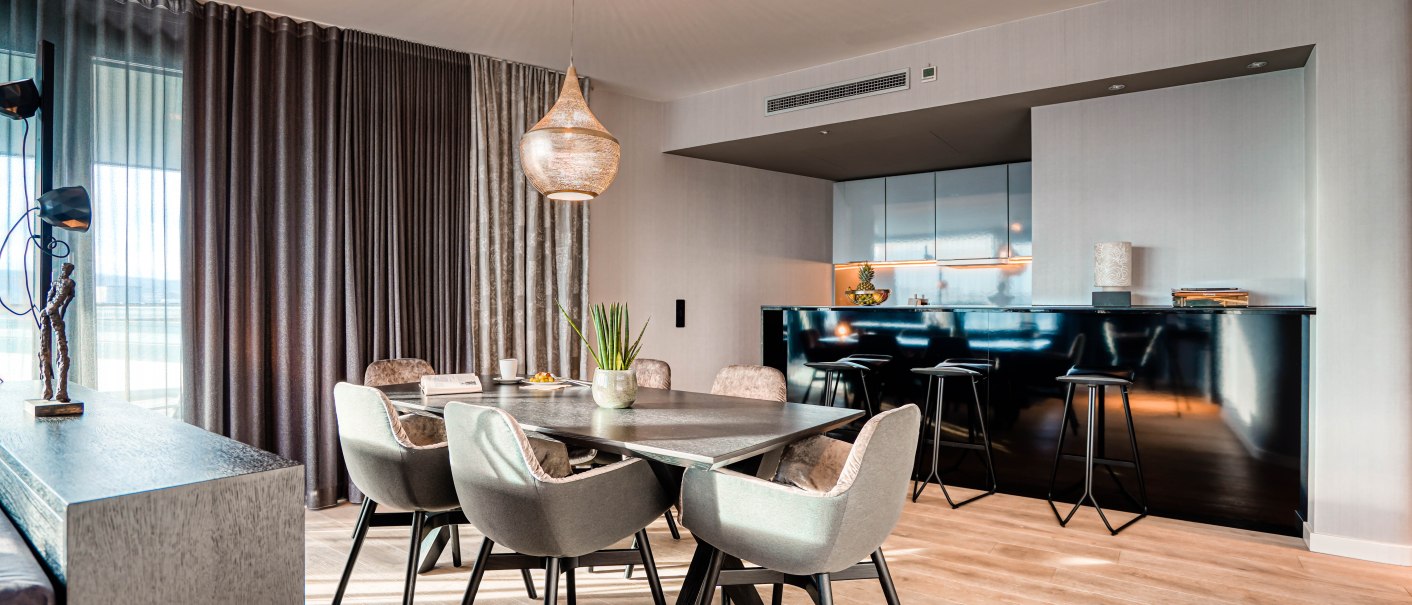 Elegante Suite mit modernem Esstisch, gepolsterten Stühlen und offener Küche. Große Fenster mit Vorhängen und stilvolle Beleuchtung., © CLOUD N°7 APARTMENTS GmbH