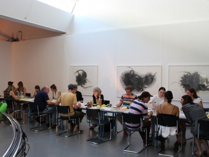 Besucher in der Kunsthalle G&ouml;ppingen sitzen an einem langen Tisch und genie&szlig;en die Atmosph&auml;re. An der Wand h&auml;ngen abstrakte Kunstwerke., &copy; Kunsthalle G&ouml;ppingen