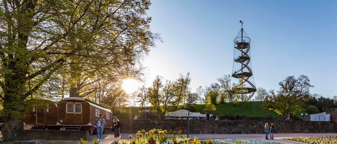 Der Killesbergturm steht in einem Park, umgeben von Bäumen. Menschen spazieren bei Sonnenuntergang. Ein Waffelstand ist sichtbar., © Stuttgart-Marketing GmbH, Werner Dieterich Der Killesbergturm steht in einem Park, umgeben von Bäumen. Menschen spazieren bei Sonnenuntergang. Ein Waffelstand ist sichtbar., © Stuttgart-Marketing GmbH, Werner Dieterich