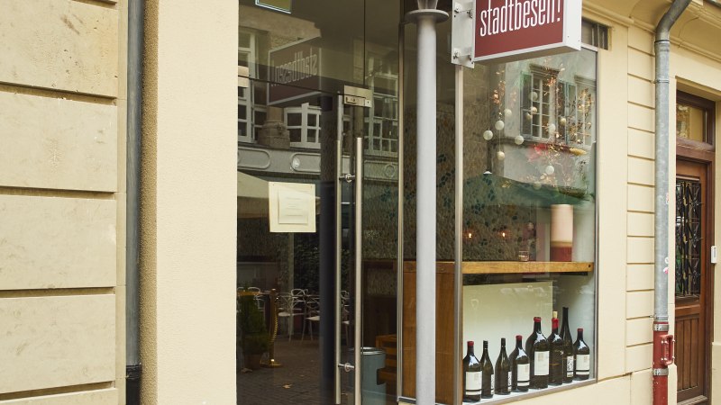 Eingang eines Geschäfts mit dem Schild 'Stadtbesen'. In der Vitrine stehen Weinflaschen. Eine rote Leuchtreklame ist an der Wand angebracht., © Stuttgart-Marketing GmbH, Sarah Schmid
