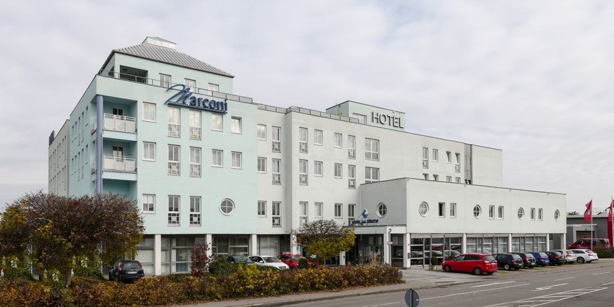 Mehrst&ouml;ckiges Hotel mit dem Namen Marconi, helle Fassade, geparkte Autos und B&auml;ume im Vordergrund., &copy; Hotel S&uuml;dtor
