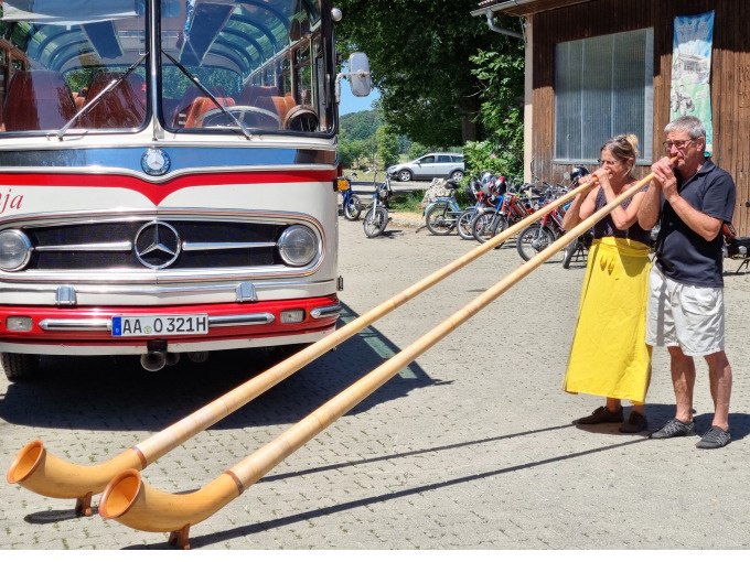 Ein Oldtimerbus steht auf einem Platz. Zwei Personen spielen Alphörner vor dem Bus. Fahrräder sind im Hintergrund zu sehen., © SwabianTravel Ein Oldtimerbus steht auf einem Platz. Zwei Personen spielen Alphörner vor dem Bus. Fahrräder sind im Hintergrund zu sehen., © SwabianTravel