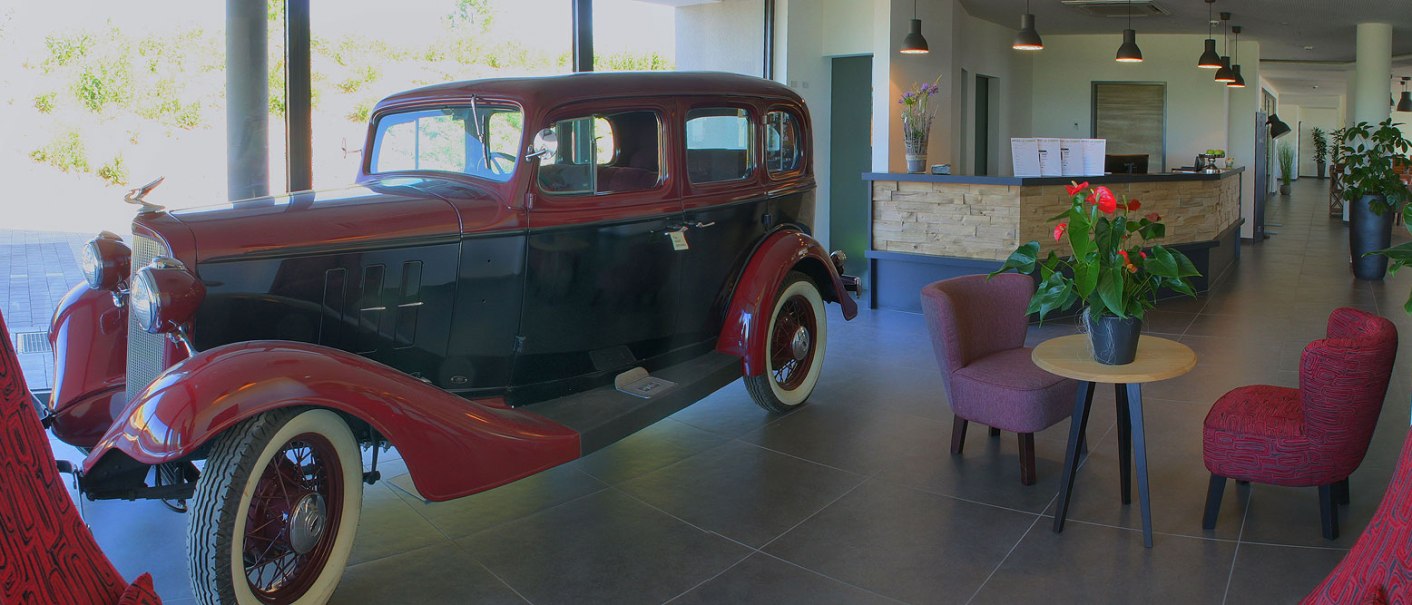 Ein Oldtimer in einer modernen Hotellobby mit Rezeption, Pflanzen und Sitzgelegenheiten., © TOMAS