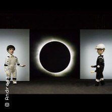 Zwei Puppen in kontrastierenden Outfits stehen vor einer Sonnenfinsternis auf einer B&uuml;hne. Die Szene wirkt dramatisch und geheimnisvoll., &copy; links im Bild