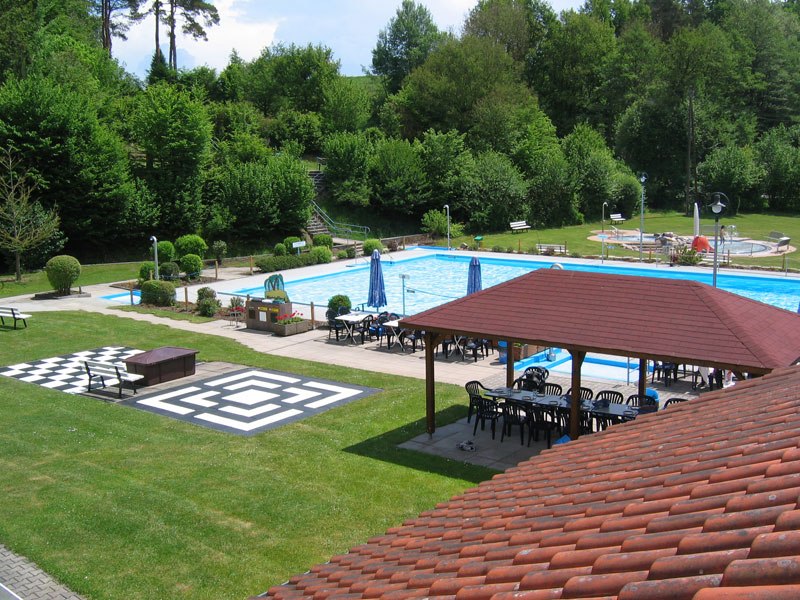 Ein Freibad mit Schwimmbecken, umgeben von Bäumen. Es gibt Sitzbereiche mit Sonnenschirmen und einen überdachten Pavillon., © FVFS Ein Freibad mit Schwimmbecken, umgeben von Bäumen. Es gibt Sitzbereiche mit Sonnenschirmen und einen überdachten Pavillon., © FVFS