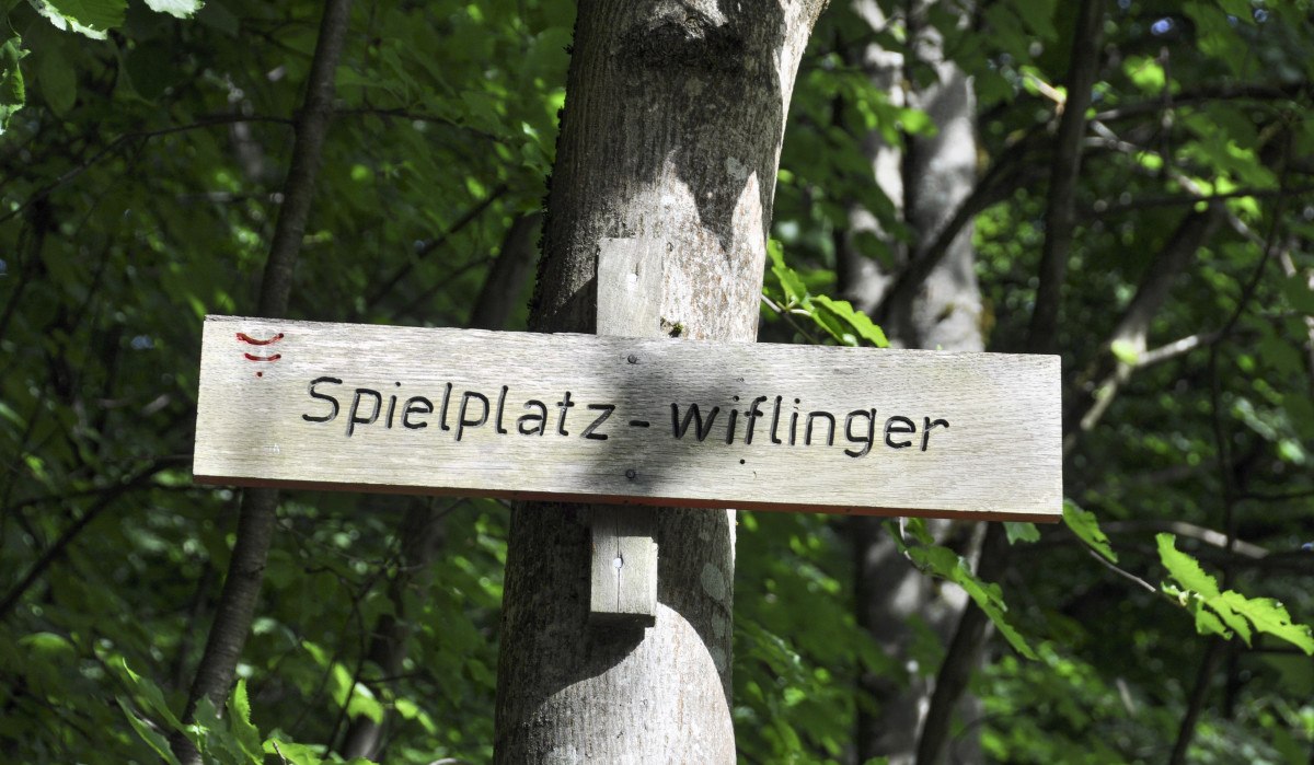 Ein Holzschild mit der Aufschrift 'Spielplatz - wiflinger' ist an einem Baum im Wald befestigt. Ein Holzschild mit der Aufschrift 'Spielplatz - wiflinger' ist an einem Baum im Wald befestigt.