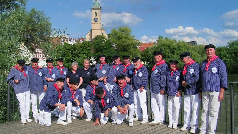 Eine Gruppe von Menschen in maritimer Kleidung posiert auf einem Steg. Im Hintergrund ist eine Kirche mit Turmuhr zu sehen., &copy; Neckar-Knurrh&auml;hne