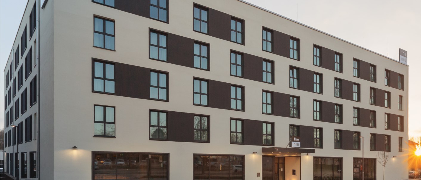 Moderne Hotelaußenfassade mit vielen Fenstern und einem Schild mit der Aufschrift 'the niu'., © Novum Management GmbH Moderne Hotelaußenfassade mit vielen Fenstern und einem Schild mit der Aufschrift 'the niu'., © Novum Management GmbH