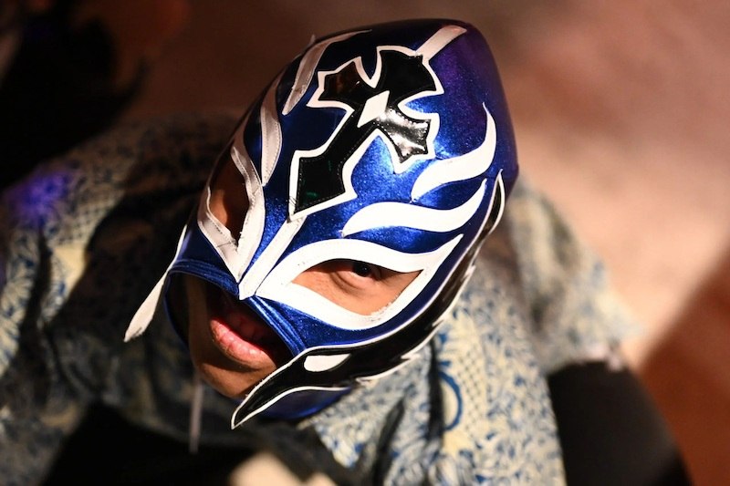 Person trägt eine blaue Lucha-Libre-Maske mit weißen und schwarzen Verzierungen und blickt nach oben., © Kulturhaus Schwanen Person trägt eine blaue Lucha-Libre-Maske mit weißen und schwarzen Verzierungen und blickt nach oben., © Kulturhaus Schwanen