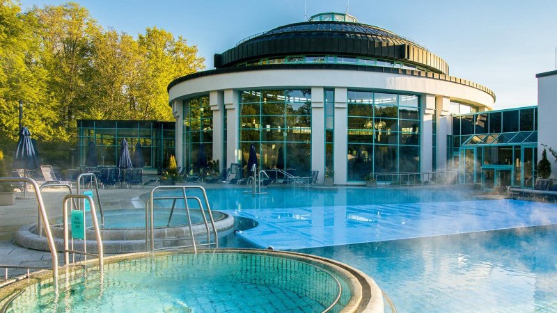 Die Mineraltherme Böblingen zeigt einen dampfenden Außenpool vor einem modernen, runden Gebäude mit großen Glasfenstern., © Stuttgart-Marketing GmbH, Sarah Schmid Die Mineraltherme Böblingen zeigt einen dampfenden Außenpool vor einem modernen, runden Gebäude mit großen Glasfenstern., © Stuttgart-Marketing GmbH, Sarah Schmid