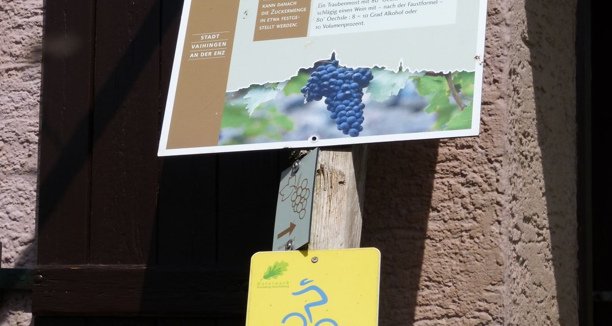 Ein Schild erklärt die Mostwaage nach Oechsle, darunter gelbe Wegweiser für Radfahrer auf einem Holzpfosten., © Land der 1000 Hügel - Kraichgau-Stromberg Ein Schild erklärt die Mostwaage nach Oechsle, darunter gelbe Wegweiser für Radfahrer auf einem Holzpfosten., © Land der 1000 Hügel - Kraichgau-Stromberg