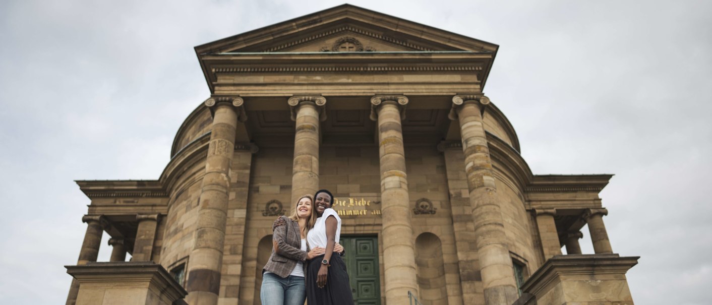 Zwei Personen umarmen sich lächelnd vor der imposanten Fassade der Grabkapelle Stuttgart mit ihren Säulen., © Stuttgart-Marketing GmbH, wpsteinheisser