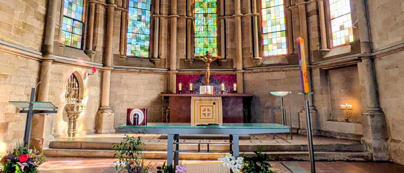 Kirchenaltar im Chorraum mit Kruzifix, Kerzen und farbigen Glasfenstern in einer gotischen Kirche., &copy; St. Katharina Stuttgart