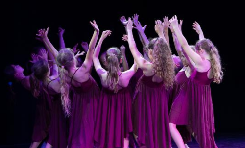 Kinder in lila Kleidern tanzen synchron auf einer Bühne. Sie haben die Arme erhoben und sind von hinten zu sehen, in einem lila Licht beleuchtet., © Kunstschule Labyrinth Kinder in lila Kleidern tanzen synchron auf einer Bühne. Sie haben die Arme erhoben und sind von hinten zu sehen, in einem lila Licht beleuchtet., © Kunstschule Labyrinth