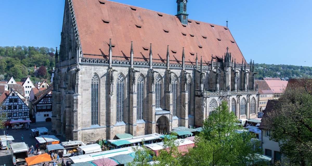 Das Heilig Kreuz Münster mit gotischer Architektur, umgeben von Marktständen und Fachwerkhäusern, unter einem klaren blauen Himmel., © Hostrup Fotografie Das Heilig Kreuz Münster mit gotischer Architektur, umgeben von Marktständen und Fachwerkhäusern, unter einem klaren blauen Himmel., © Hostrup Fotografie