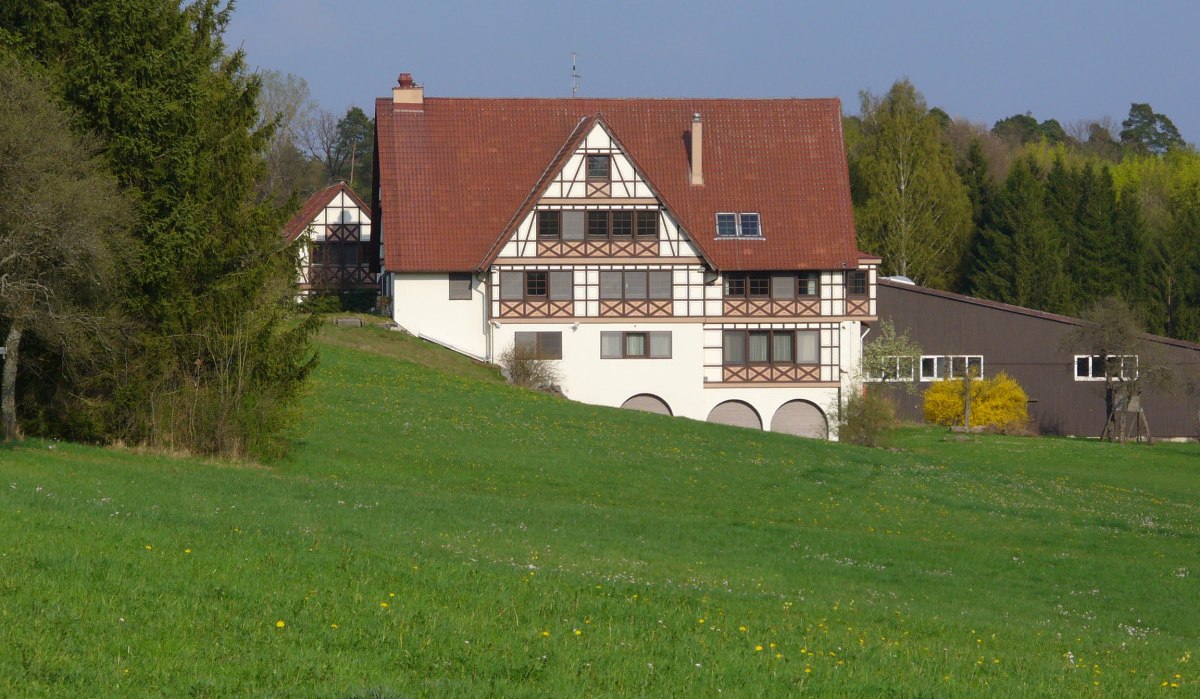 Fachwerkhaus mit rotem Dach auf einer grünen Wiese, umgeben von Bäumen und blühenden Sträuchern., © Naturfreunde Holzgerlingen/Altdorf
