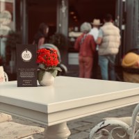 Ein weißer Tisch mit roter Blume steht vor der Eisdiele 'Ciao Giulia'. Im Hintergrund sind Menschen zu sehen., © Ciao Giulia Ein weißer Tisch mit roter Blume steht vor der Eisdiele 'Ciao Giulia'. Im Hintergrund sind Menschen zu sehen., © Ciao Giulia