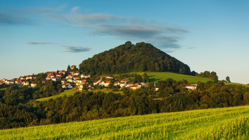 Der Berg Hohenstaufen erhebt sich hinter einem Dorf, umgeben von grünen Feldern und Bäumen, unter einem klaren blauen Himmel., © Landkreis Göppingen