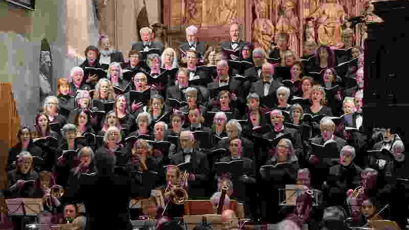 Ein großer Chor und Orchester führen in einer Kirche ein Konzert auf. Der Chor steht vor einem kunstvoll geschnitzten Altar., © Evangelische Kirchengemeinde Winnenden