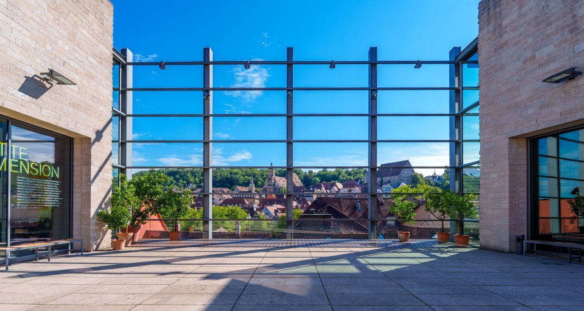 Terrasse der Kunsthalle Würth mit Glasfassade, Topfpflanzen und Blick auf die Altstadt von Schwäbisch Hall unter blauem Himmel., © Michael Kuehneisen Terrasse der Kunsthalle Würth mit Glasfassade, Topfpflanzen und Blick auf die Altstadt von Schwäbisch Hall unter blauem Himmel., © Michael Kuehneisen