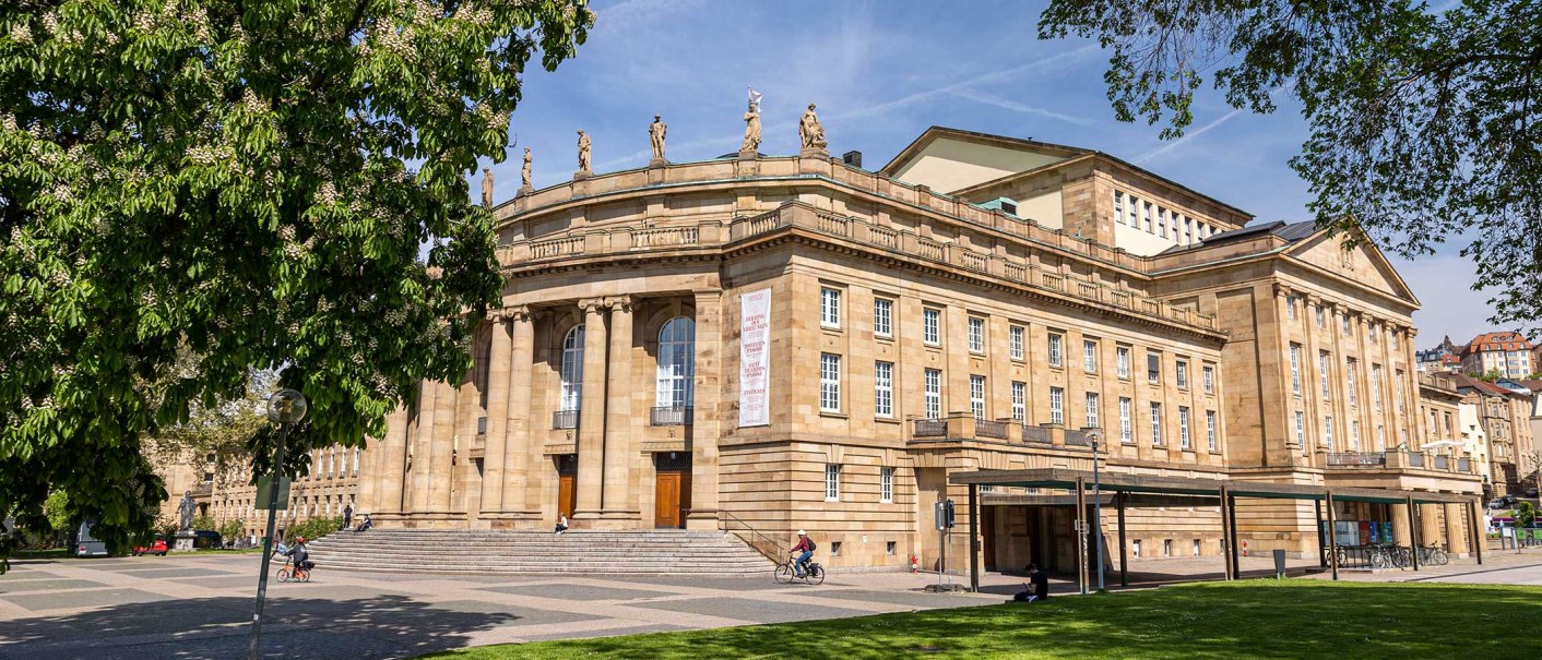 Die Staatsoper Stuttgart bei sonnigem Wetter, umgeben von grünen Bäumen und einem Radfahrer im Vordergrund., © Stuttgart Marketing GmbH, Sarah Schmid Die Staatsoper Stuttgart bei sonnigem Wetter, umgeben von grünen Bäumen und einem Radfahrer im Vordergrund., © Stuttgart Marketing GmbH, Sarah Schmid