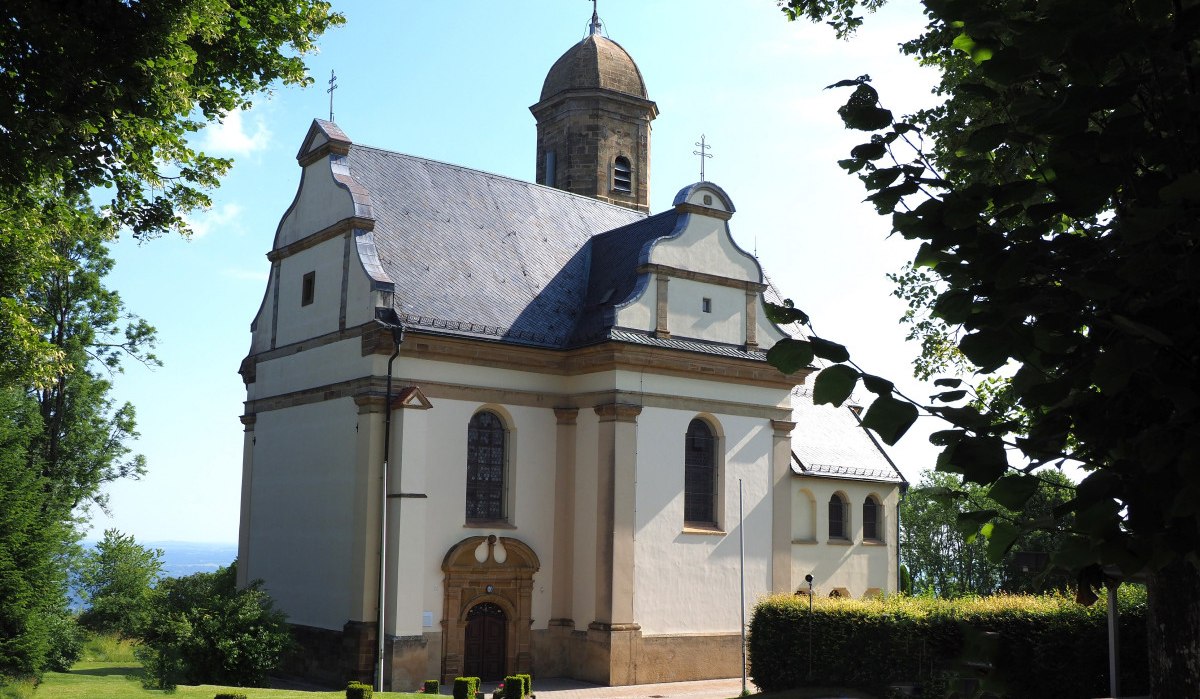 Die St. Maria Wallfahrtskirche Hohenrechberg steht inmitten grüner Bäume. Das Gebäude hat eine helle Fassade und einen markanten Turm., © Foto: Walter Laible