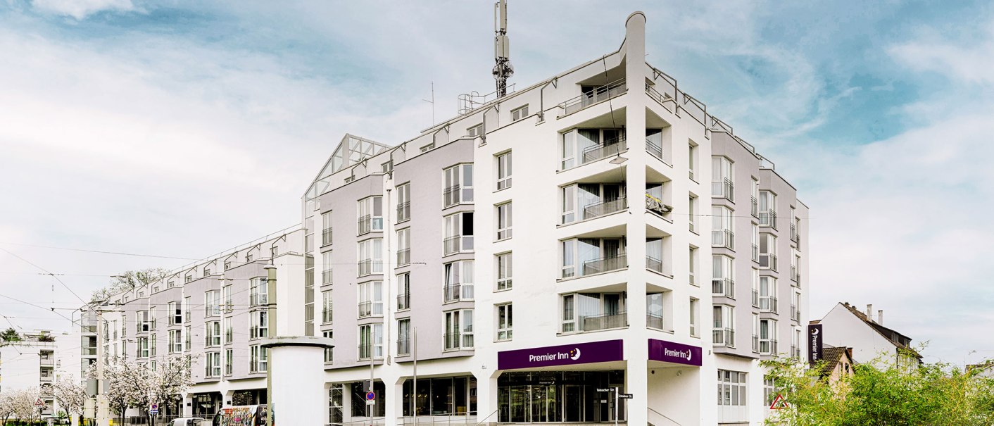 Modernes Hotelgebäude mit mehreren Stockwerken, Balkonen und einem Premier Inn Schild. Der Himmel ist leicht bewölkt., © Premier Inn Germany