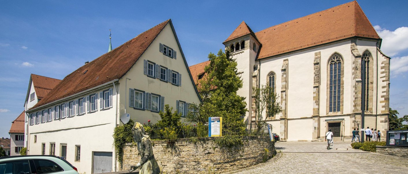 Historische Gebäude im Stiftshof Backnang, darunter eine Kirche mit gotischen Fenstern und ein Haus mit blauen Fensterläden, bei sonnigem Wetter., © Stuttgart-Marketing GmbH, Sarah Schmid