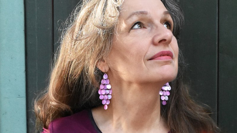 Eine Frau mit langen Haaren tr&auml;gt auff&auml;llige lila Ohrringe und blickt nach oben. Sie tr&auml;gt ein buntes Oberteil., &copy; Dieselstrasse Kulturzentrum e.V.
