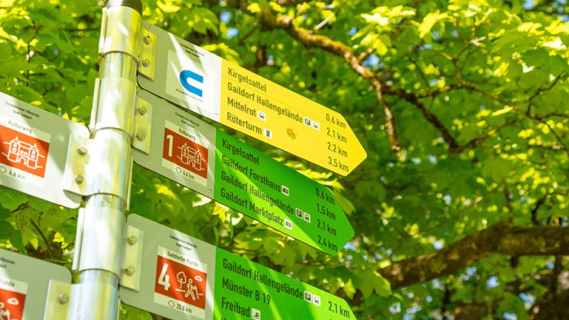Wegweiser für Rundwanderwege in Gaildorf mit Entfernungsangaben, umgeben von grünem Laub.