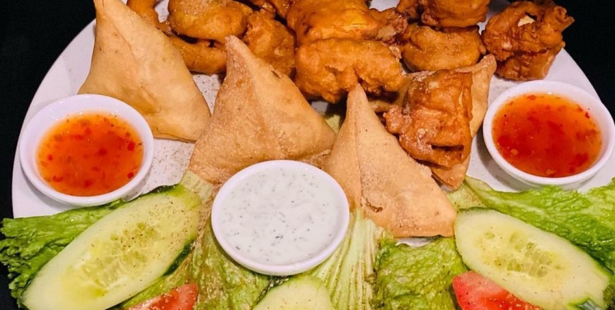 Ein Teller mit Samosas, Pakoras, Salatblättern, Gurken, Tomaten und zwei Dips., © Taj Mahal Bad Urach