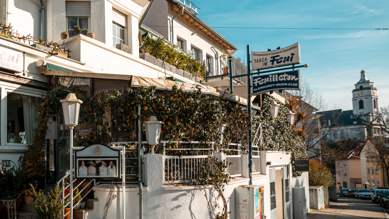 Ein Restaurant mit dem Namen 'Tasca im Feui', das portugiesische und spanische Spezialitäten anbietet. Daneben ein Schild für 'Feuilleton', einen Kleinkunst- und Musikclub., © Stuttgart-Marketing GmbH, Sarah Schmid Ein Restaurant mit dem Namen 'Tasca im Feui', das portugiesische und spanische Spezialitäten anbietet. Daneben ein Schild für 'Feuilleton', einen Kleinkunst- und Musikclub., © Stuttgart-Marketing GmbH, Sarah Schmid