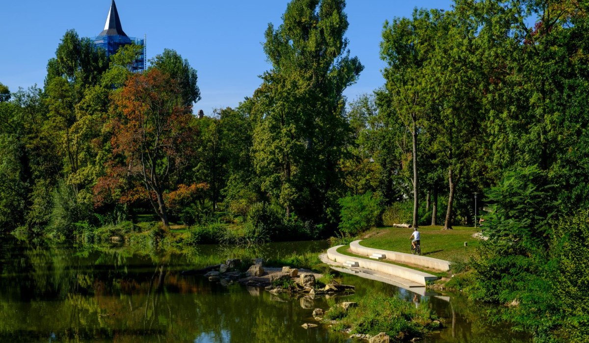Ein grüner Park mit einem Teich, Bäumen und einem Turm im Hintergrund. Eine Person mit Fahrrad auf einem Weg., © WTM GmbH Waiblingen Ein grüner Park mit einem Teich, Bäumen und einem Turm im Hintergrund. Eine Person mit Fahrrad auf einem Weg., © WTM GmbH Waiblingen