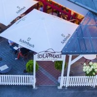 Terrasse mit weißen Sonnenschirmen und Holzmöbeln, umgeben von einem weißen Zaun. Menschen sitzen an Tischen, dekoriert mit Blumen., © Hotel Waldhorn