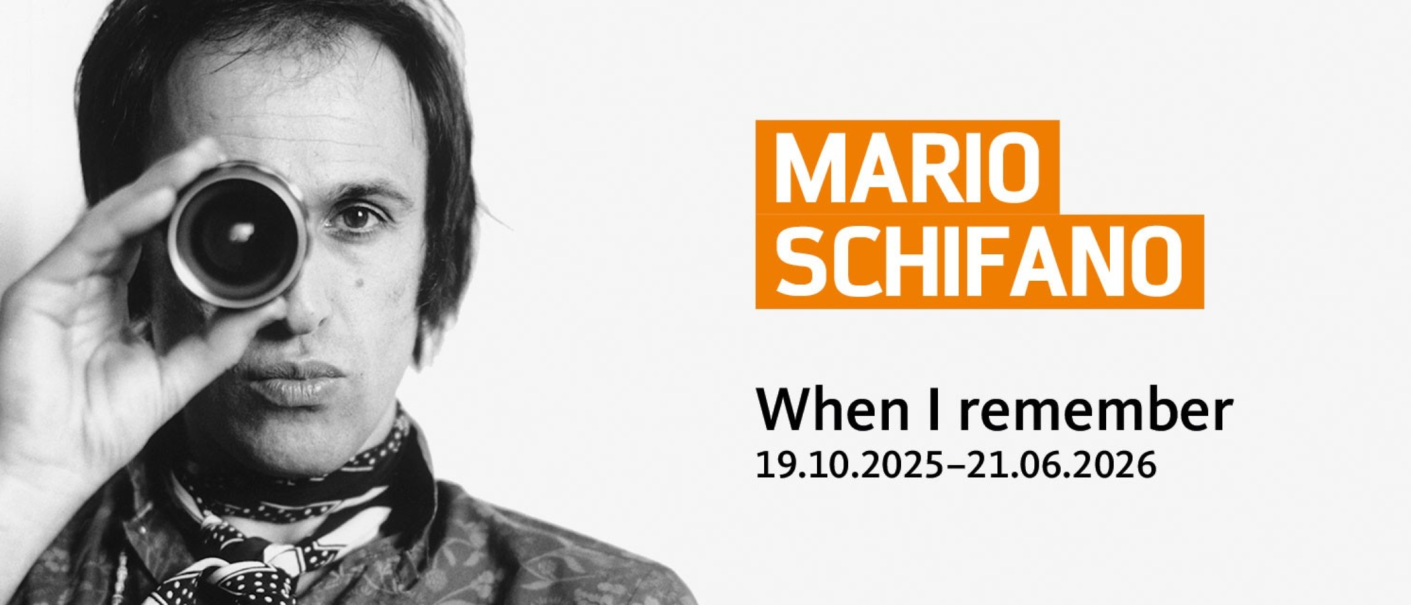 Schwarz-weiß Bild eines Mannes, der durch ein Objektiv schaut. Rechts steht "Mario Schifano" in orange und "When I remember" mit Ausstellungsdaten., © SCHAUWERK Sindelfingen_Foto: Patrizia Ruspoli