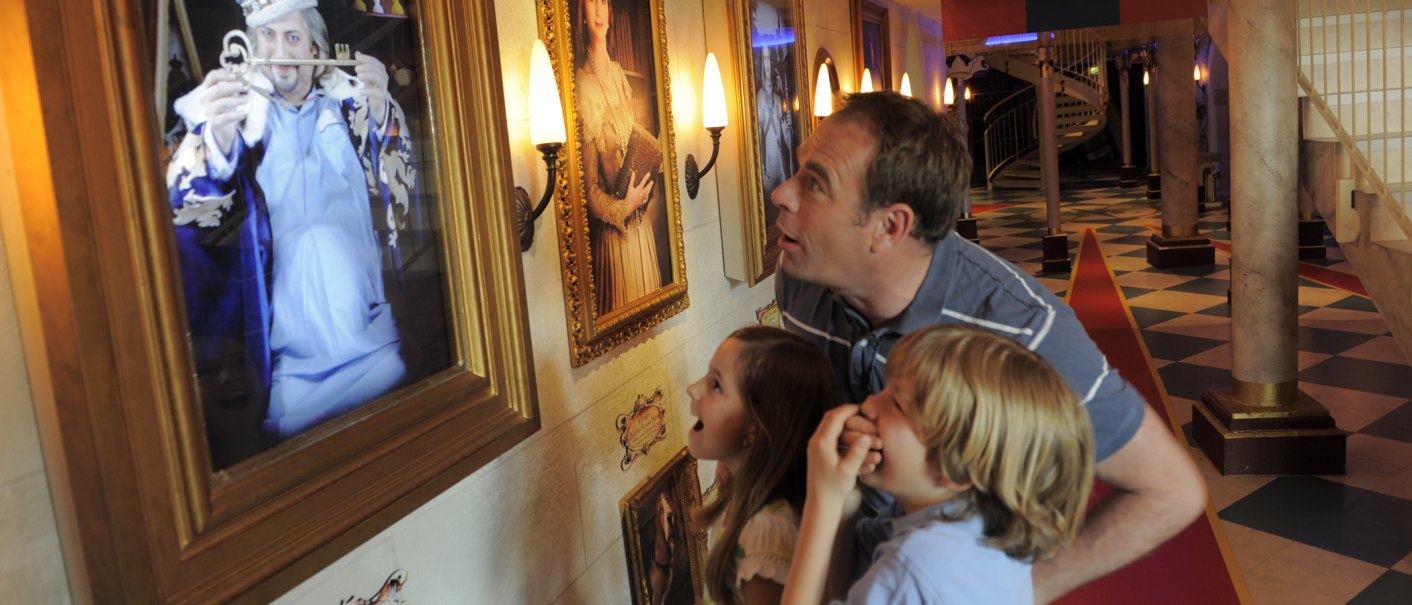 Ein Mann und zwei Kinder schauen fasziniert auf ein interaktives Bild in einem Museum, das einen Zauberer mit einem Schlüssel zeigt., © Sensapolis Sindelfingen