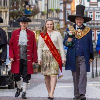 F&uuml;nf Personen in historischen Kost&uuml;men, darunter eine Frau mit Sch&auml;rpe, gehen eine gepflasterte Stra&szlig;e entlang. Sie tragen H&uuml;te und M&auml;ntel., &copy; Stadt Besigheim
