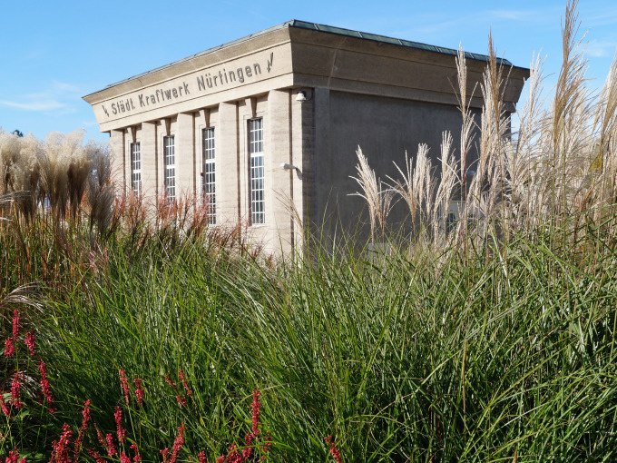 Das alte Kraftwerk N&uuml;rtingen steht majest&auml;tisch hinter hohen Gr&auml;sern und bl&uuml;henden Pflanzen, ein Zeugnis industrieller Architektur., &copy; Stadt N&uuml;rtingen