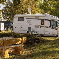 Wohnmobile auf einem sonnigen Campingplatz, umgeben von Bäumen. Im Vordergrund steht ein Holztisch mit Bänken., © Stuttgart-Marketing GmbH, Sarah Schmid