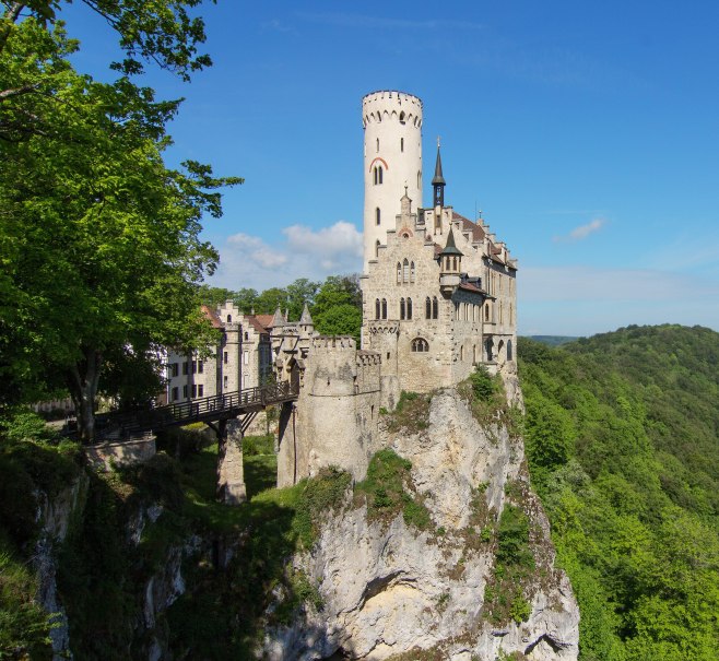 Schloss Lichtenstein thront auf einem Felsen, verbunden durch eine Br&uuml;cke, umgeben von &uuml;ppigem Wald und blauem Himmel., &copy; Armin Dieter