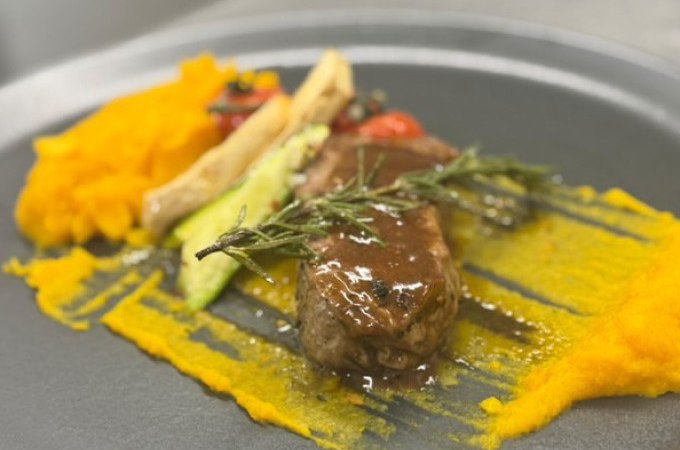 Ein kunstvoll angerichtetes Gericht mit Fleisch, Kürbispüree und Gemüse auf einem grauen Teller, dekoriert mit Rosmarin., © Cool-Tours StattReisen Ein kunstvoll angerichtetes Gericht mit Fleisch, Kürbispüree und Gemüse auf einem grauen Teller, dekoriert mit Rosmarin., © Cool-Tours StattReisen