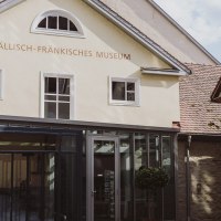 Eingang des Hällisch-Fränkischen Museums in Schwäbisch Hall, mit moderner Glasfassade und historischen Gebäuden im Hintergrund., © Nico Kurth