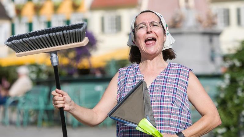 Frau in kariertem Hemd und Kopftuch hält Besen und Kehrschaufel, singt oder spricht begeistert im Freien., © © T&E, Benjamin Stollenberg Frau in kariertem Hemd und Kopftuch hält Besen und Kehrschaufel, singt oder spricht begeistert im Freien., © © T&E, Benjamin Stollenberg