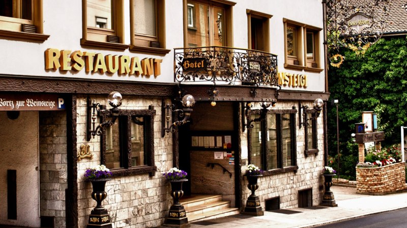 Eingang des Hotels Zur Weinsteige mit dekorativen Elementen, großen Fenstern und Restaurantbeschilderung. Blumen schmücken den Eingangsbereich., © Hotel Zur Weinsteige Eingang des Hotels Zur Weinsteige mit dekorativen Elementen, großen Fenstern und Restaurantbeschilderung. Blumen schmücken den Eingangsbereich., © Hotel Zur Weinsteige